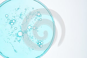 Transparent drops of cosmetic product serum gel in petri dish. Liquid texture with bubbles on blue background. Skincare