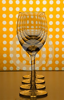 Transparent empty wine glasses one behind the other and yellow orange background with white spots.