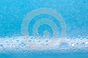 Transparent foaming blue liquid with oxygen bubbles texture close up. Abstract surfactant cosmetic background.