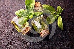 A transparent glass bottle of basil essential oil with fresh basil leaves on rustic table