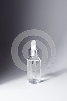 Transparent glass bottle with silver and white pipette in light on grey background mockup. Facial serum in dropper