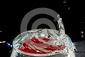 Transparent glass bowl, filled with water, with red reflection and splashing drops. Splash Effect