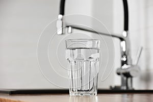 Transparent glass of clean filtering water on wooden table in kitchen interior. Tap with purified water with an osmosis