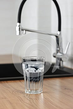 Transparent glass of clean filtering water on wooden table in kitchen interior. Tap with purified water with an osmosis