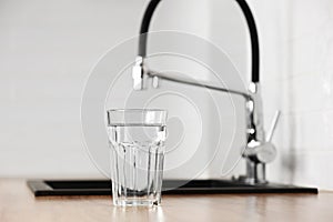 Transparent glass of clean filtering water on wooden table in kitchen interior. Tap with purified water with an osmosis