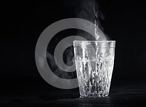 Transparent glass cup with swell the boiling water into it. The vapor from the top. Black background.