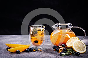 Transparent glass cup and teapot with exotic fruit tea, on a black and gray background