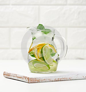 Transparent glass decanter with slices of lemon, lime and mint leaves on a white table, detox