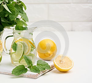 Transparent glass decanter with slices of lemon, lime and mint leaves on a white table, detox. Behind the ingredients for the