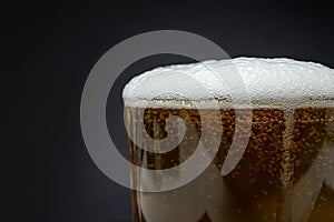 Transparent glass filled with golden beer and thin foam, side view close up crop, soft focus texture