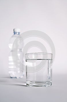 A transparent glass full of water. near a bottle of mineral water.