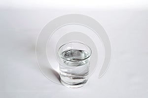 A transparent glass full of water. near a bottle of mineral water.