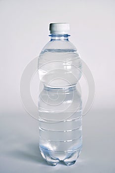 A transparent glass full of water. near a bottle of mineral water.