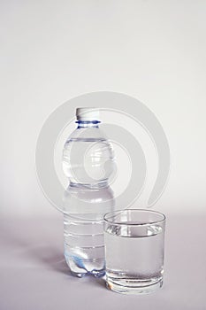 A transparent glass full of water. near a bottle of mineral water.