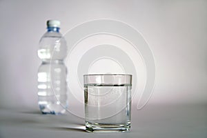 A transparent glass full of water. near a bottle of mineral water.