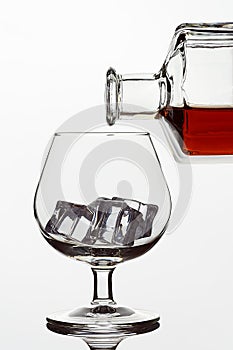 Transparent glass glass with ice cubes and a bottle of whiskey or cognac or brandy on a white isolated background