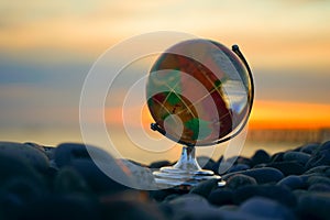 transparent glass globe ball on pebble beach background. crystal glass globe on sunrise beach of the Black sea. sunset sky. sign,