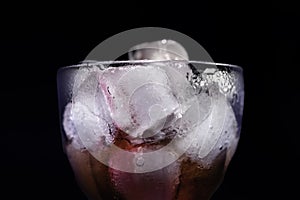 A transparent glass with ice and drink in the neon lights on black background. Cocktail, party, and night life concept