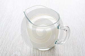 Transparent glass jug with milk on table