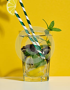 Transparent glass with lemonade, mint leaves, lemon slices and blackberries in the middle