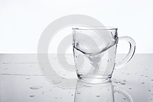 Transparent glass mug with water on light surface with water drops. Water in the form of tornado inside mug