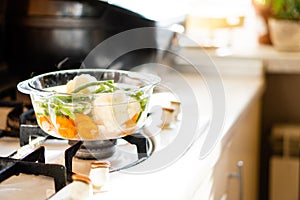 Transparent glass pan with vegetable soup, fresh hot food boils on the stove