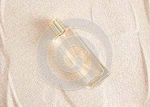 transparent glass perfume bottle with golden cap withiut label on sand background