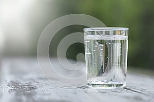 Transparent glass with pure mineral water on a green natural blurred background. outdoor