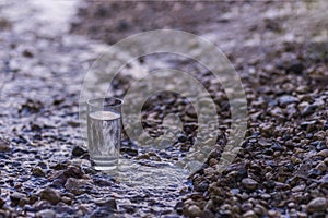 A transparent glass of pure natural cold water stands on a rock in a mountain stream.