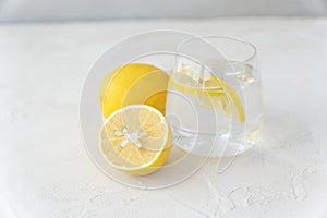 Transparent glass with pure water, lemon slices,  whole lemon and half of it lie on light background