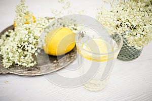 A transparent glass with a slice of lemon and a bouquet of elderberry in a vase on the summer terrace. Soft soft drink