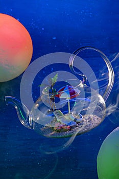 Transparent glass tea pot with sand, sunbed, umbrella, flip-flops, lifebuoy inside floats in space between red and green