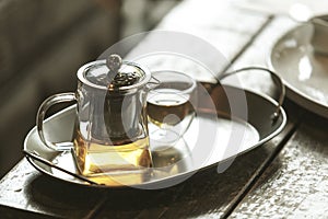 Transparent glass teapot and cup of tea on the stainless steel tray