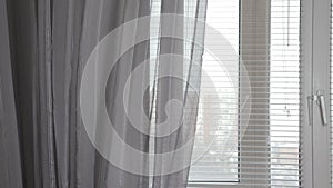 A transparent gray curtain on the window with blinds in the morning, gently moved by the wind
