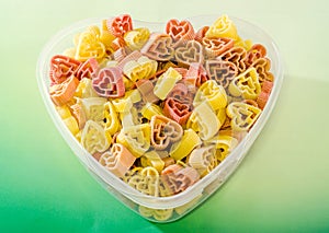 Transparent heart shape vase (bowl) filled with colored (red, yellow an orange) heart shape pasta, colored degradee background