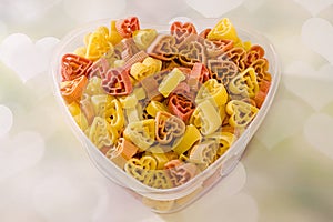 Transparent heart shape vase (bowl) filled with colored (red, yellow an orange) heart shape pasta, colored degradee background