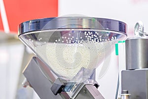 A transparent hopper with polypropylene granules is part of the injection molding machine. White granules are used to