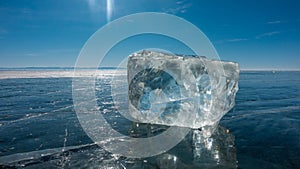 A transparent ice crystal lies on the smooth blue surface of a frozen lake.