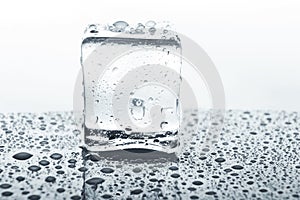 Transparent ice cube on glass with water drops