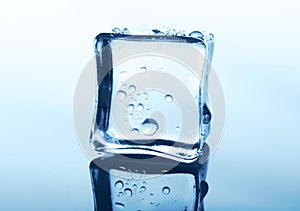 Transparent ice cube with reflection on blue glass with water drops