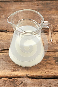 Transparent jug with milk on wooden background.