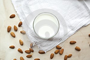 Transparent mug full of milk on white cotton napkin and scattered nuts almonds. Almond milk, rustic style, top view