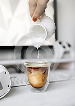 Transparent mug of hot coffee with cream on a white workplace of a programmer and gamer.