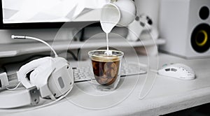 Transparent mug of hot coffee with cream on a white workplace of a programmer and gamer.
