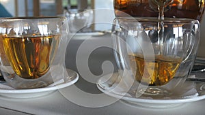 Transparent mug stands and then hot ceylon tea is poured into it from glass teapot. Waiter at the restaurant. Two cups