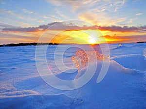 Transparent piece of ice on the snow against the backdrop of a winter sunset