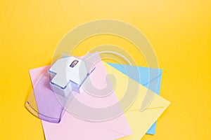 transparent plastic computer mouse and paper colored envelopes on a yellow background,