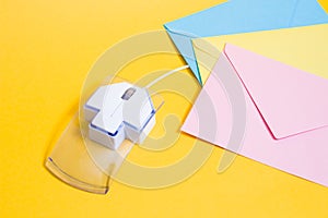 transparent plastic computer mouse and paper colored envelopes on a yellow background