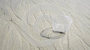 Transparent plastic cup on the beach make pollution at  the ocean, for Environmental conservation concept. Recycle Garbage on sand