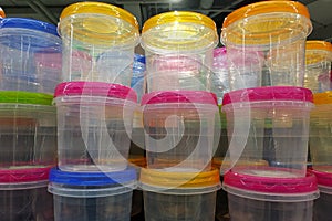 Transparent plastic food containers with multi-colored lids stacked in a stack.